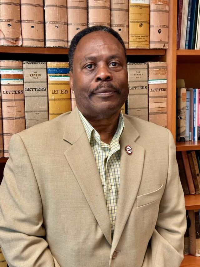 horace highlight in a tan suit in front of a full bookshelf