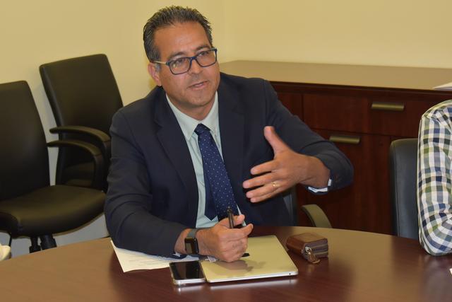 a man wearing a blue suit a tie with a notebook and cellphone on the table in front of him