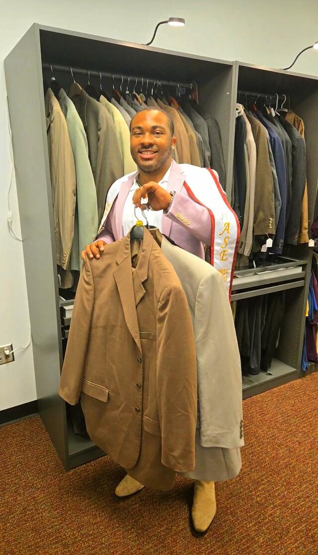 cameron baldwin a young black man holds suits donated to the marauder boutique