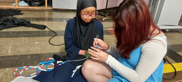 a young person wearing a hijab makes a jump rope with a volunteer