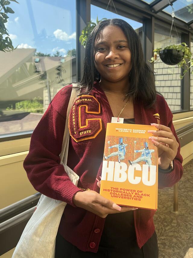 meiyah hill holding a book about historically black colleges and universities and wearing a central state university sweater