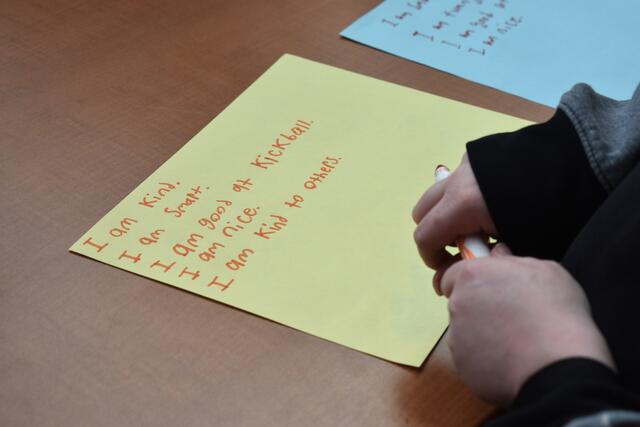 a young person's hands holding a marker over a sheet of paper with written affirmations