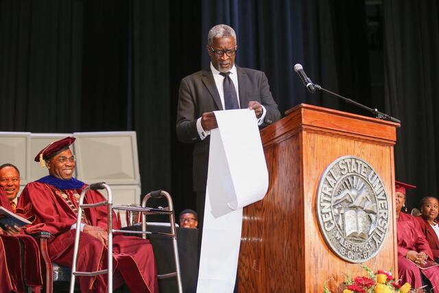 dr. allen level holds a long scroll of paper at the podium