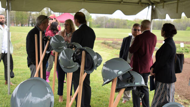 shovels and hats at groundbreaking with people in the background standing under a large tent